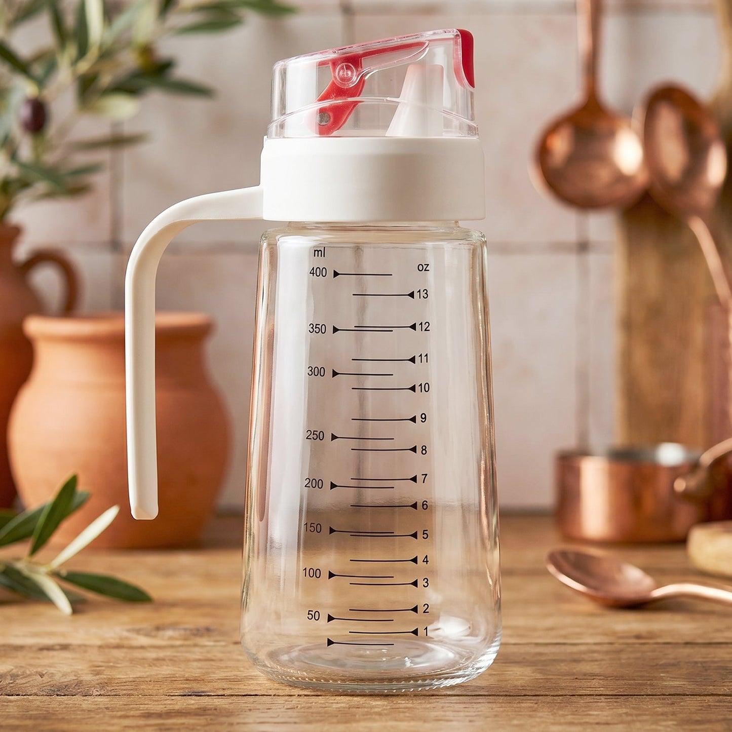 Glass Oil Dispenser Bottle 500ml with Auto-Flip Red Cap, White Side Handle and ml/oz Measurement Scale on Rustic Wooden Kitchen Counter