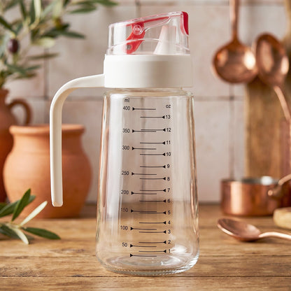 Glass Oil Dispenser Bottle 500ml with Auto-Flip Red Cap, White Side Handle and ml/oz Measurement Scale on Rustic Wooden Kitchen Counter