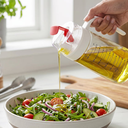 Hand Holding 500ml Glass Oil Bottle with Red Flip Cap Drizzling Olive Oil onto Arugula Salad with Cherry Tomatoes and Red Onion